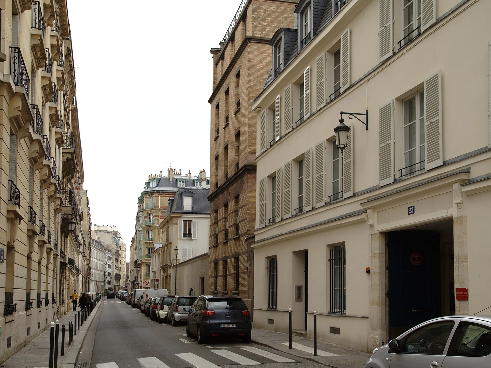 A narrow Paris street lined with pale façades, shutters and parked cars.