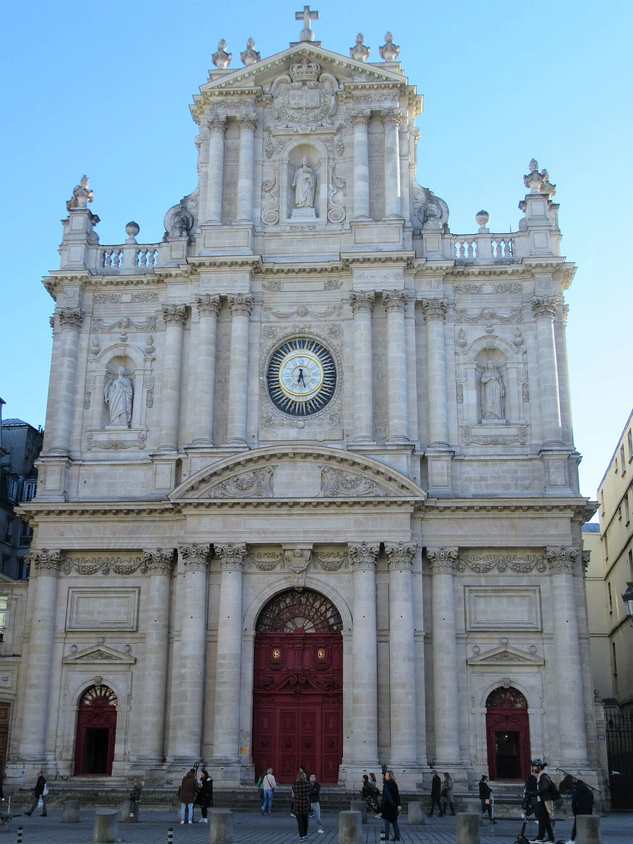 The pale stone Baroque façade and red doors of Saint-Paul-Saint-Louis beneath a blue sky.